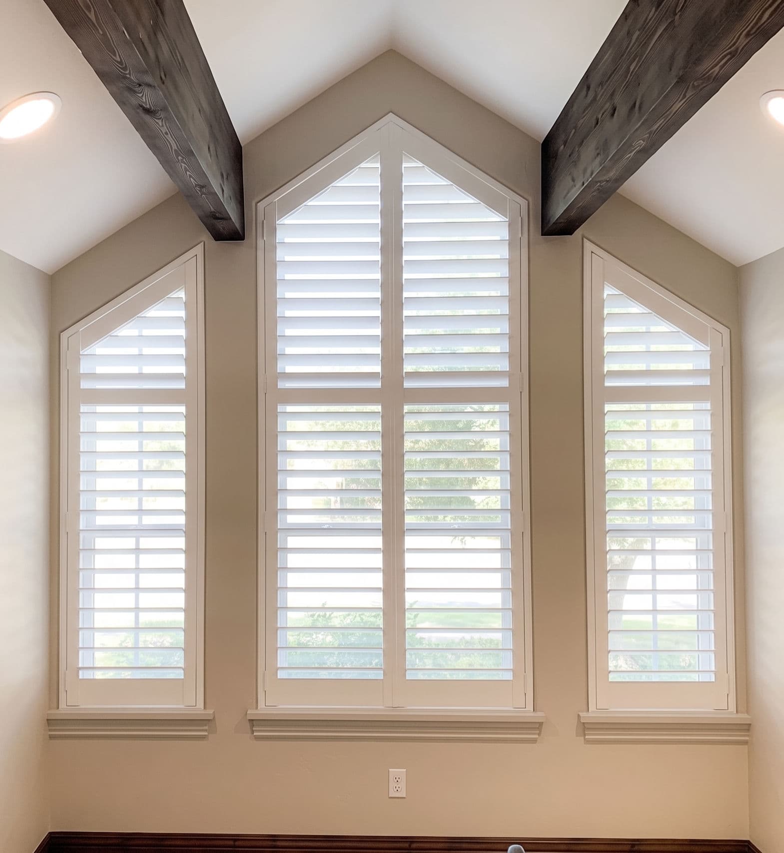 Custom plantation shutters fitted to angled-top windows with wood beam ceiling